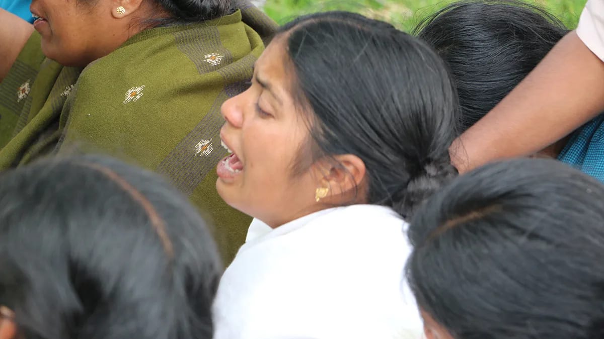 A woman singing with her eyes closed, held by other women pressed close around her.