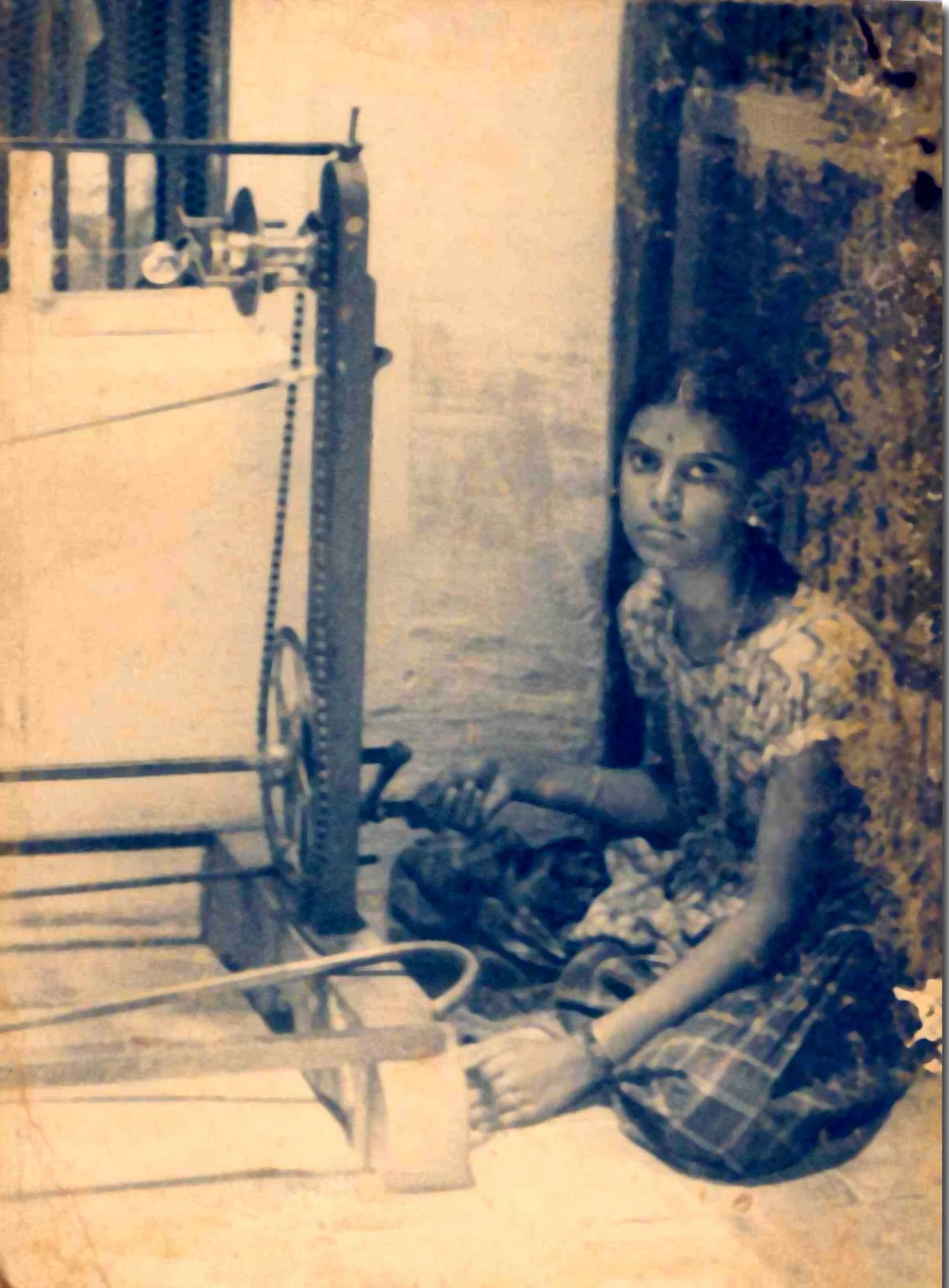 A young woman seated on the floor beside a hand-cranked string winder, in a sepia photograph from the 1940s.