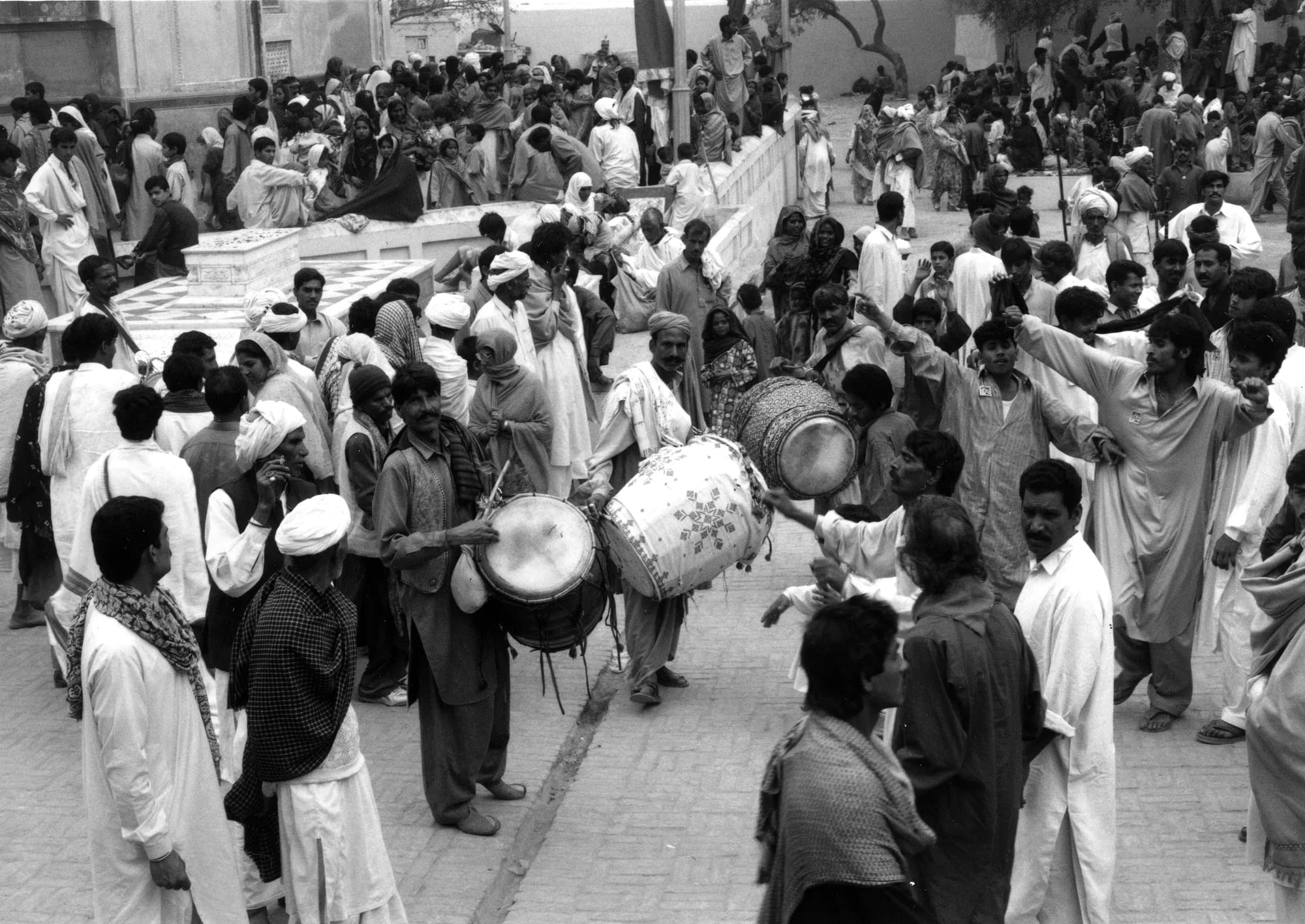 Drummers carrying large barrel drums through a dense street procession, in black and white.